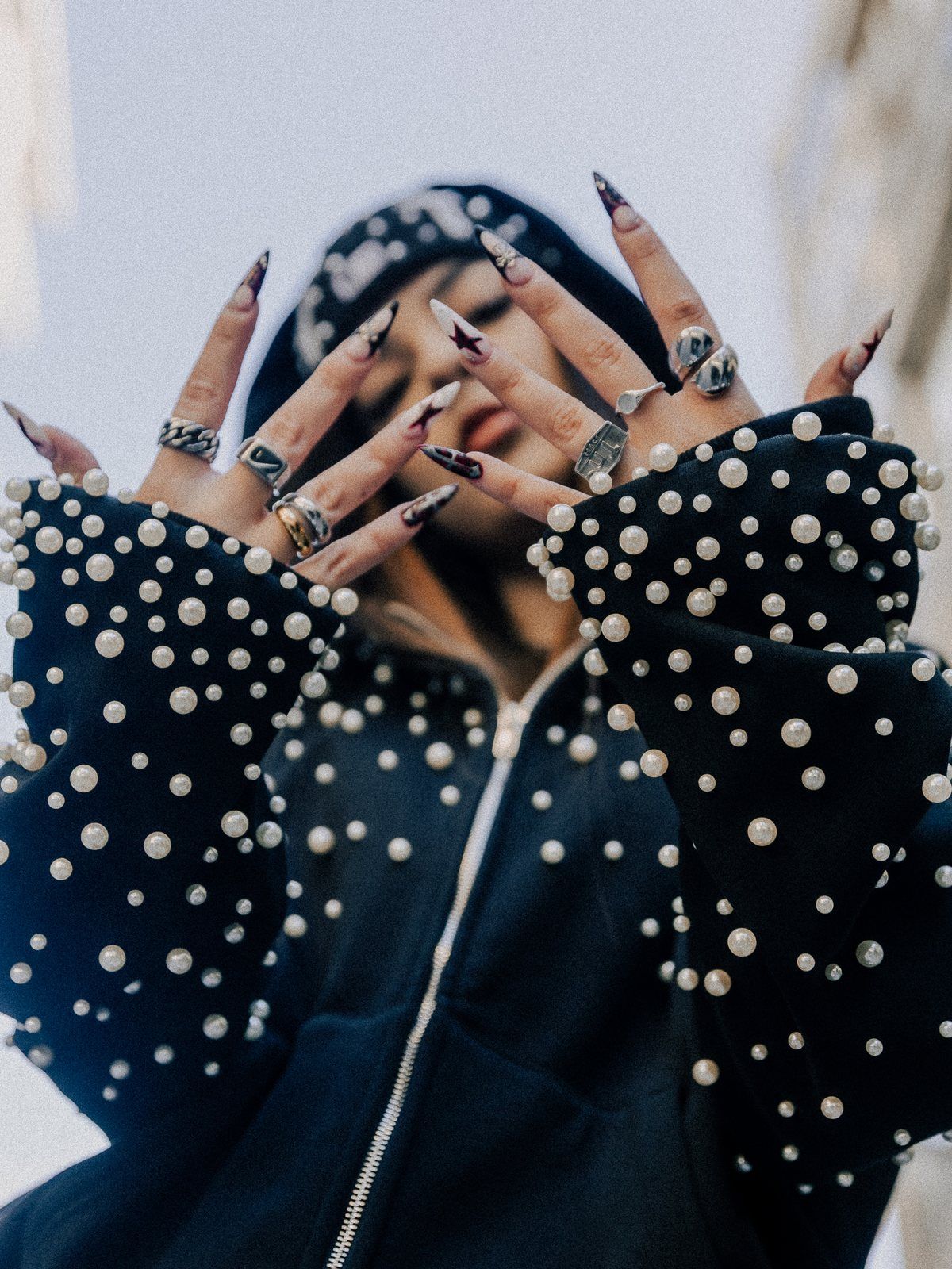 Pearl zip-up worn with a cap, hands raised to the camera