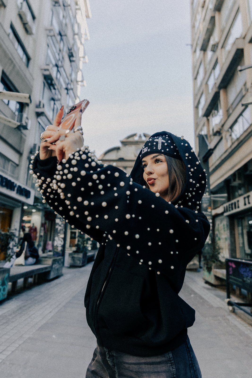 Pearl zip-up in a city street, arm raised